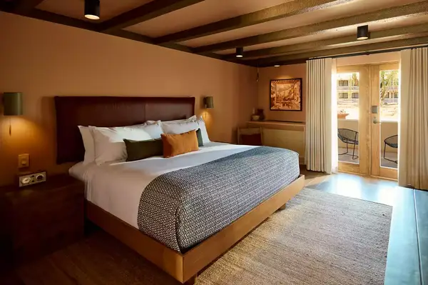 A guest room with a neatly made bed, bedside tables, and French doors leading to an outdoor patio area