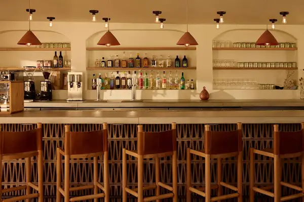 Bar area with high wooden chairs, shelves displaying various bottles and glassware, pendant lights hanging from the ceiling
