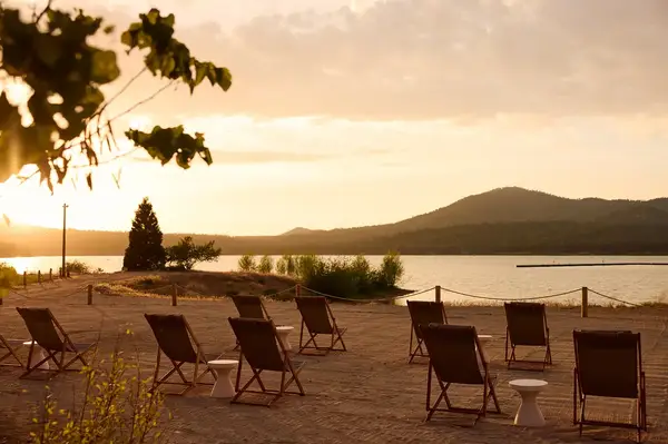 A sunny lakeside view with loungers and hills in the background