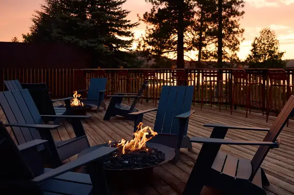 Outdoor deck with fire pits and chairs surrounded by trees and a sunset view