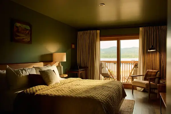 Warmly lit hotel room with a bed seating area and a balcony overlooking a scenic view