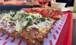 Several slices of pizza served on a red tray a partially visible person holding a bowl in background