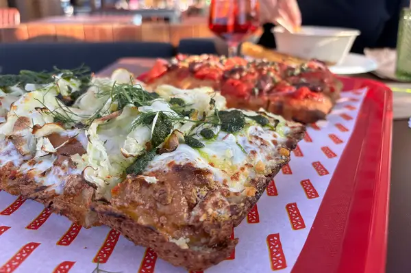 Several slices of pizza served on a red tray a partially visible person holding a bowl in background