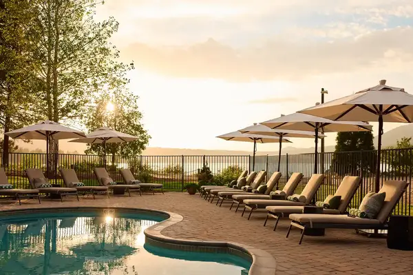 Poolside lounge chairs and umbrellas set against a sunset with a scenic backdrop and fencing