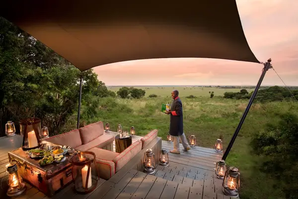 Outdoor seating area with a server holding a bottle surrounded by lanterns and a scenic landscape in the background