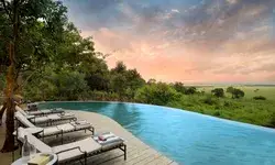 Infinity pool overlooking a scenic landscape with chairs and trees nearby