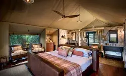 Luxury tentstyle room with a bed seating area desk and open bathroom layout featuring a safari lodge aesthetic