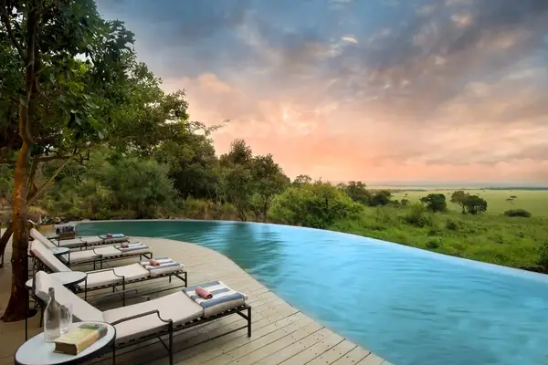 Infinity pool overlooking a scenic landscape with chairs and trees nearby