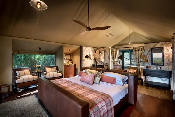 Luxury tentstyle room with a bed seating area desk and open bathroom layout featuring a safari lodge aesthetic