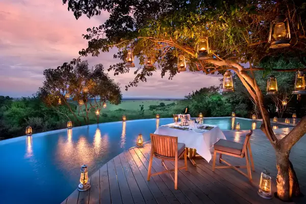 An outdoor dining setup on a deck by an infinity pool surrounded by lanterns and overlooking a scenic landscape