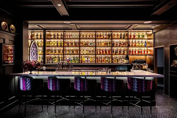 A well-lit lounge bar with an illuminated liquor shelf and purple seats at the counter