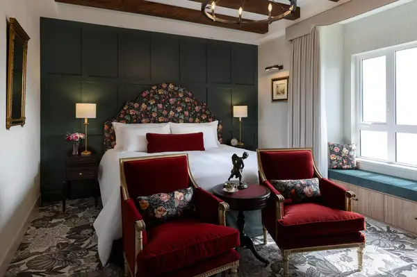 Elegant bedroom with a large bed, decorative chairs, bedside lamps, and a window seat