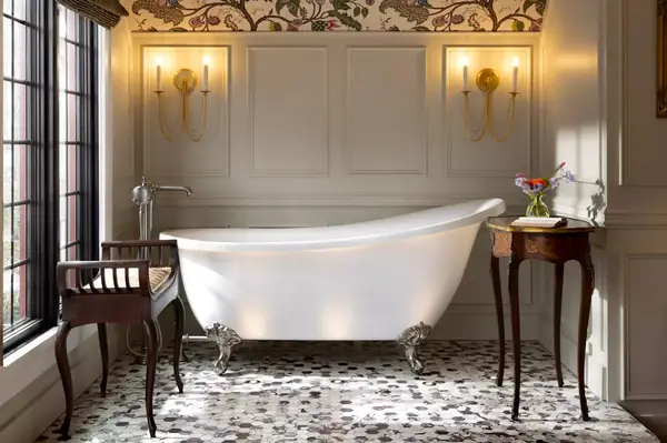 Freestanding bathtub in a classic styled bathroom with floral wallpaper, flanked by side tables
