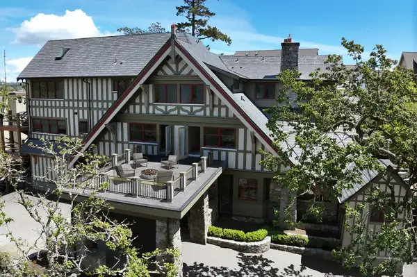 Large Tudor-style house with an outdoor seating area on a balcony, surrounded by trees