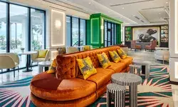 A modern lobby with vibrant decor, including a plush orange couch and animal print-themed cushions, with tables and artwork