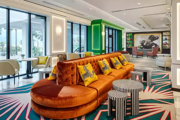 A modern lobby with vibrant decor, including a plush orange couch and animal print-themed cushions, with tables and artwork