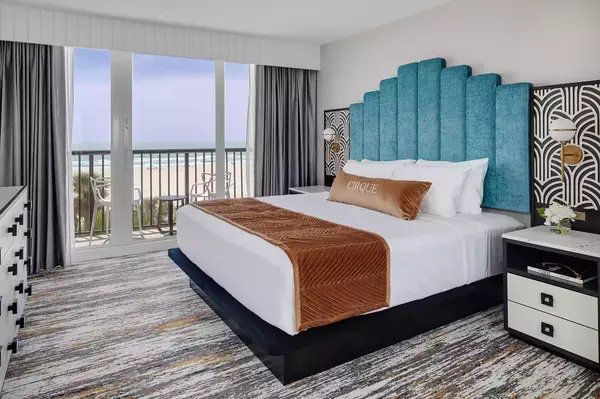 Modern guestroom with a bed and view of the beach through large windows, elegant decor and relaxing atmosphere