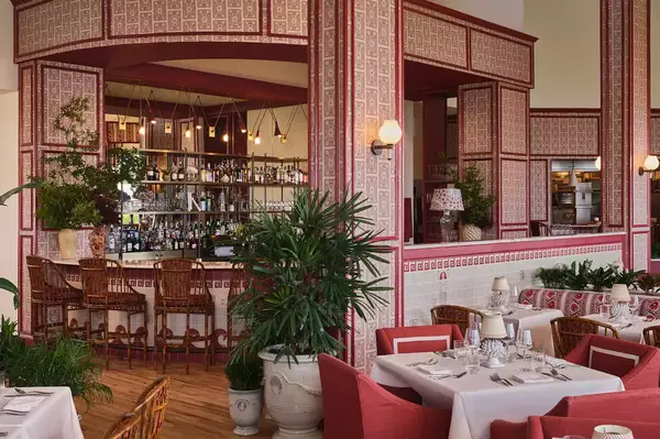 Restaurant interior with tables set for dining, a bar, and decorative plants and furnishings in an open space