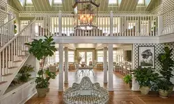 Interior lobby view with wooden floors, central seating, plants, and chairs, featuring a warm atmosphere and green accents