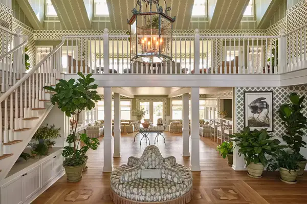 Interior lobby view with wooden floors, central seating, plants, and chairs, featuring a warm atmosphere and green accents