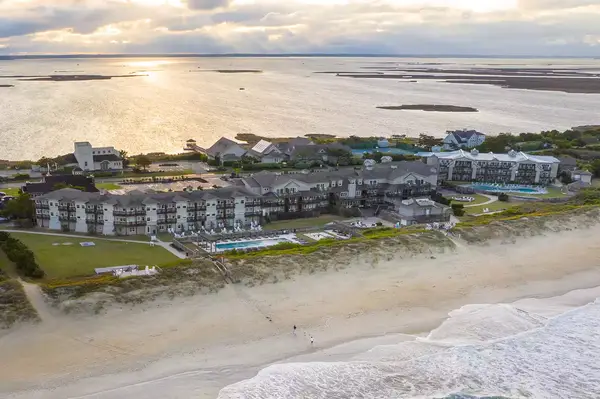 Aerial view of a resort complex along a sandy beach and open water at sunset, suggesting accommodations and leisure