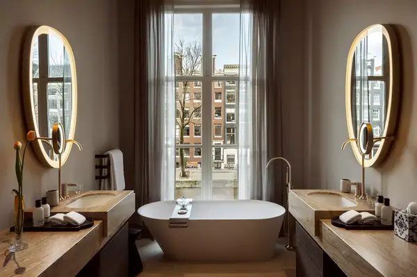 A luxurious bathroom with a freestanding bathtub centered between two vanities under a large window