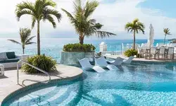 Lounge chairs in a pool on a terrace overlooking the ocean with palm trees and seating areas around