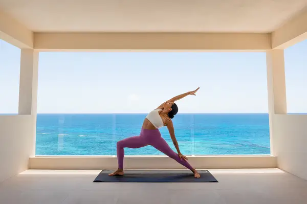 A person practicing yoga in a large room with an ocean view