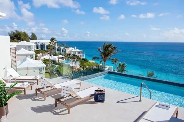 Elevated pool deck overlooking the ocean with lounge chairs and villas in the background, tropical setting