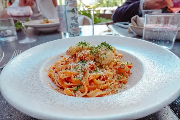 A plate of pasta garnished with herbs and surrounded by drinks on a dining table