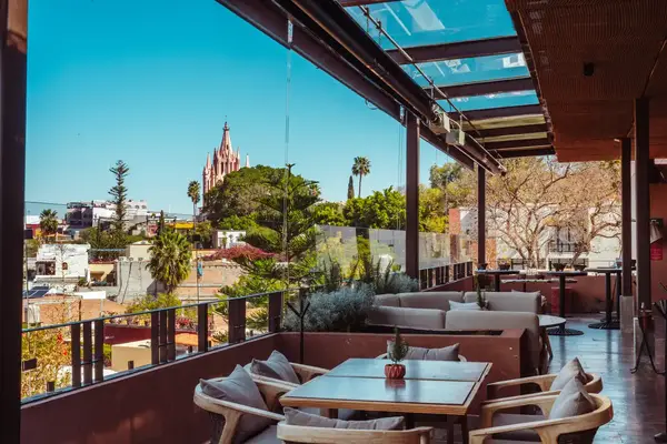 Rooftop patio view with tables, lush greenery, and a prominent church spire in the distance