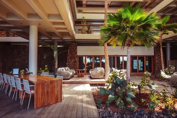 Outdoor seating area at a resort with a wooden dining table, lounge chairs, and tropical plants