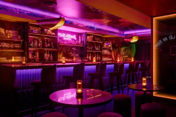 A stylish bar with neon signage and illuminated shelves, featuring tables and chairs in a lounge setting