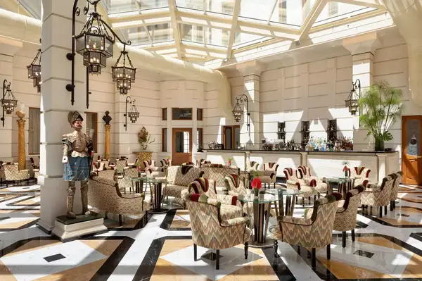 A spacious, elegant dining area with chairs and tables, ornate decor, glass ceiling, and lantern-style lighting