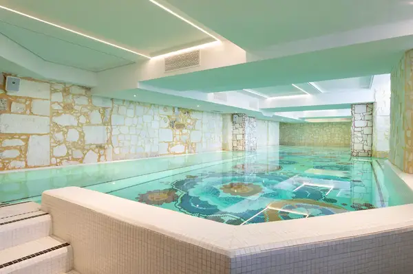 Indoor pool with mosaic-style floor designs, located in a facility with stone-textured walls and a modern ceiling