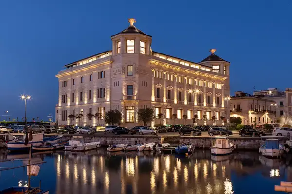 Elegant palace hotel along a marina with boats, lit up at dusk