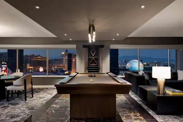 A billiards table in a suite with large windows overlooking a city skyline at night