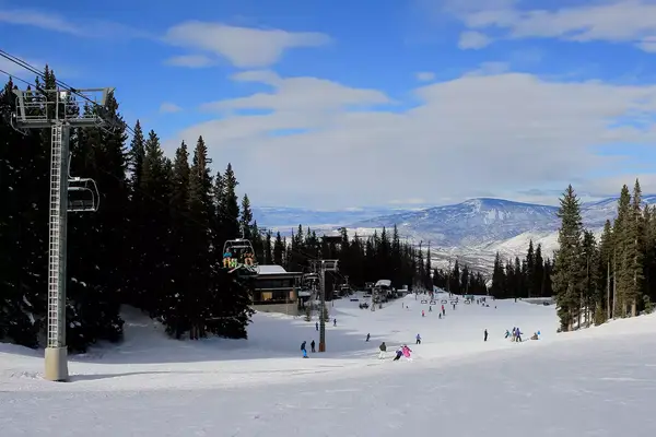 Skiers and snowboarders are skiing down to a chairlift in Snowmass