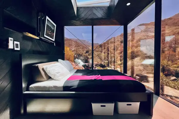 View of guest room in mirror house with black walls on one side and floor to ceiling windows on the other three sides. 