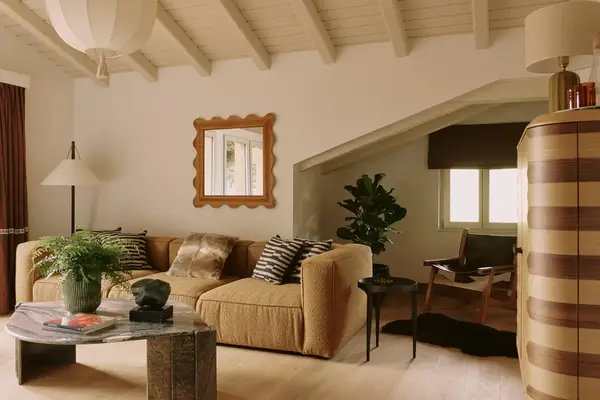 Living room with a sectional sofa, coffee table, mirror, and plant near the window in a bright space