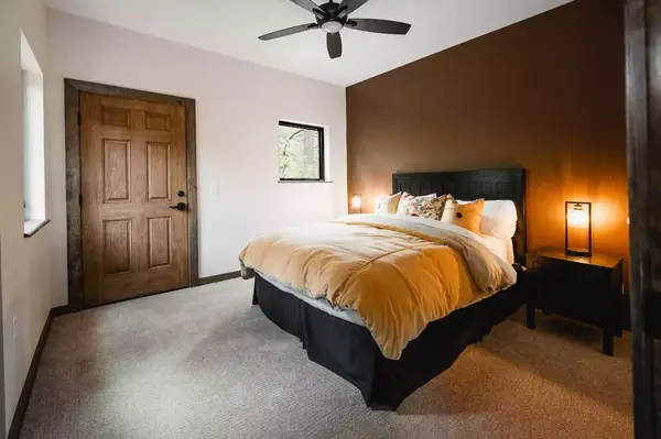 A cozy bedroom with a bed featuring plush bedding, a wooden door, a ceiling fan, and warm lighting on nightstands, spacious and inviting