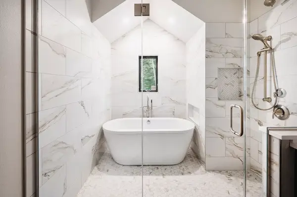 Bathtub in modern marble bathroom with a glass shower enclosure and small window