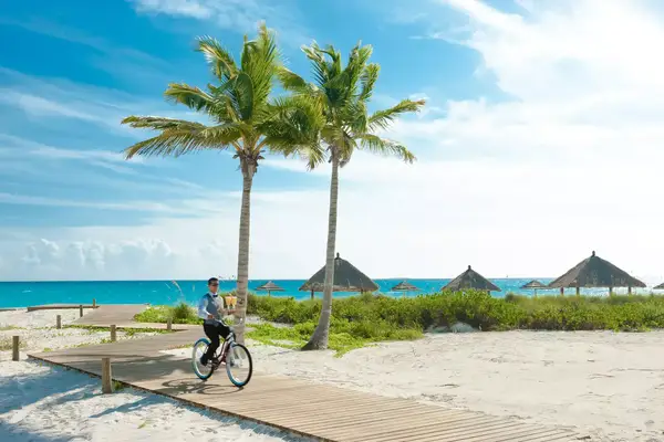 A hotel butler rides a bike on a beach boardwalk