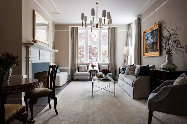 A parlor room with sofas a coffee table fireplace and a chandelier with large windows allowing natural light to fill the space