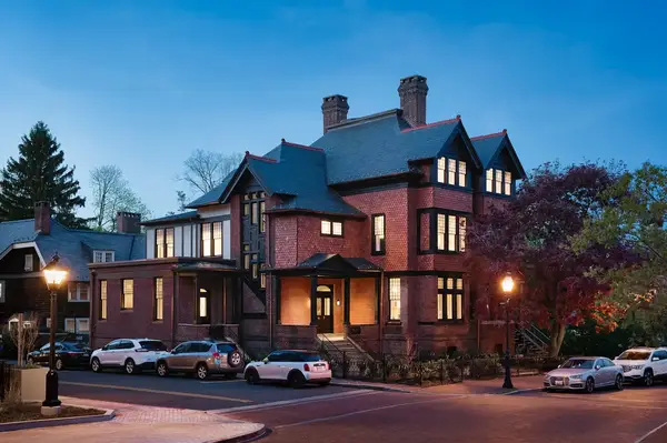 An elegant brick building with multiple windows and chimneys at a corner intersection during the evening