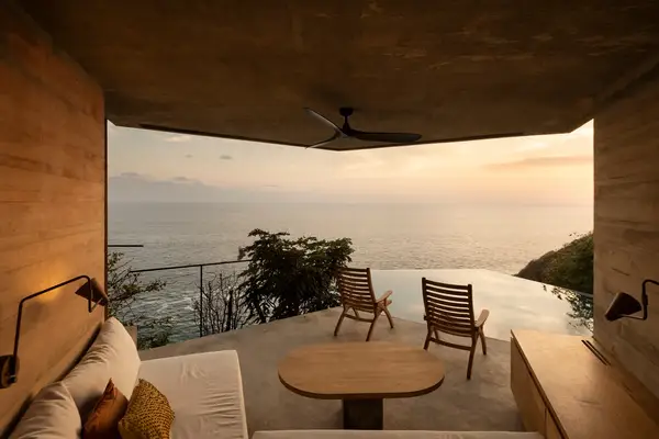 A luxury room with an ocean view featuring an infinity pool and wooden chairs on the terrace