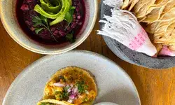 Plated food including two tacos with garnishes a dip in a bowl and a serving of flatbreads with a napkin in a basket