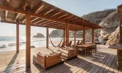 A wooden deck with chairs and tables overlooking a beach and ocean waves