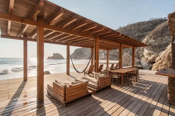 A wooden deck with chairs and tables overlooking a beach and ocean waves