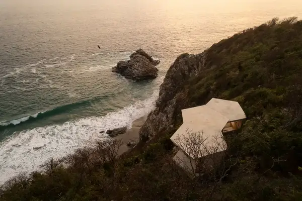 A modern hexagonal building on a coastal cliff overlooking the ocean and beach below